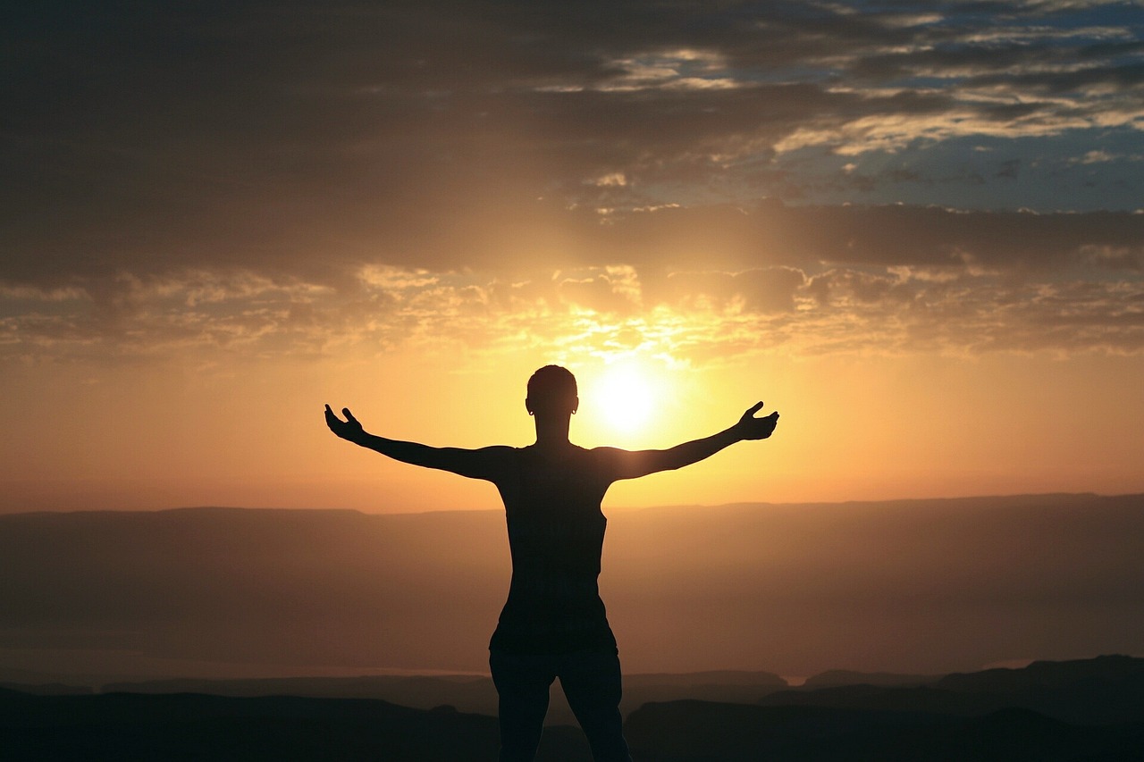 Mujer en actitud de gratitud en una puesta de sol.