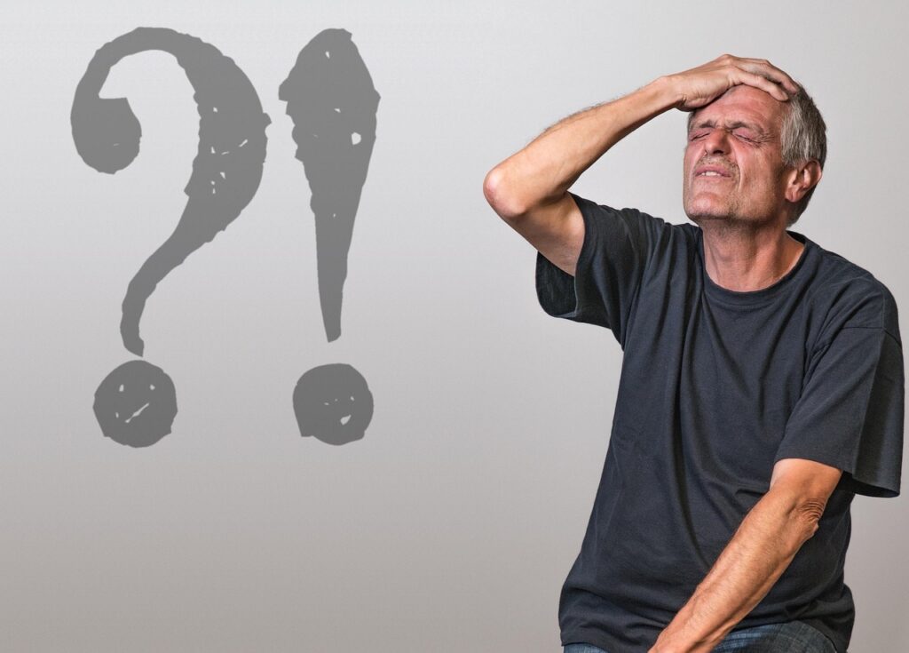 Signo interrogativo y signo admirativo y un hombre apretando los ojos y llevándose la mano a la cabeza. 